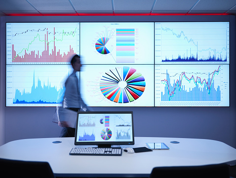 Businessman walking in front of graphs on screen