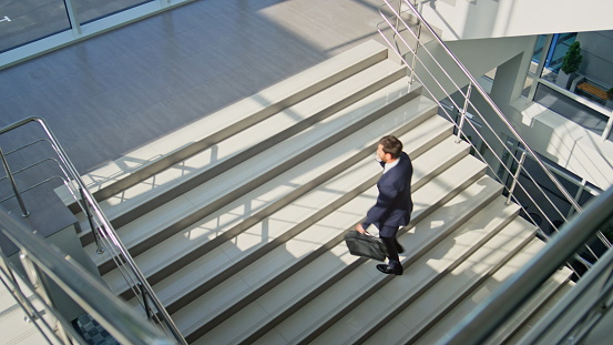 business man climbing stairs in modern office talking on smartphone.